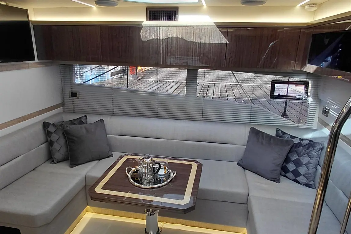 Luxurious yacht interior featuring a grey sofa with cushions, a wooden table with a tea set, and panoramic views outside.